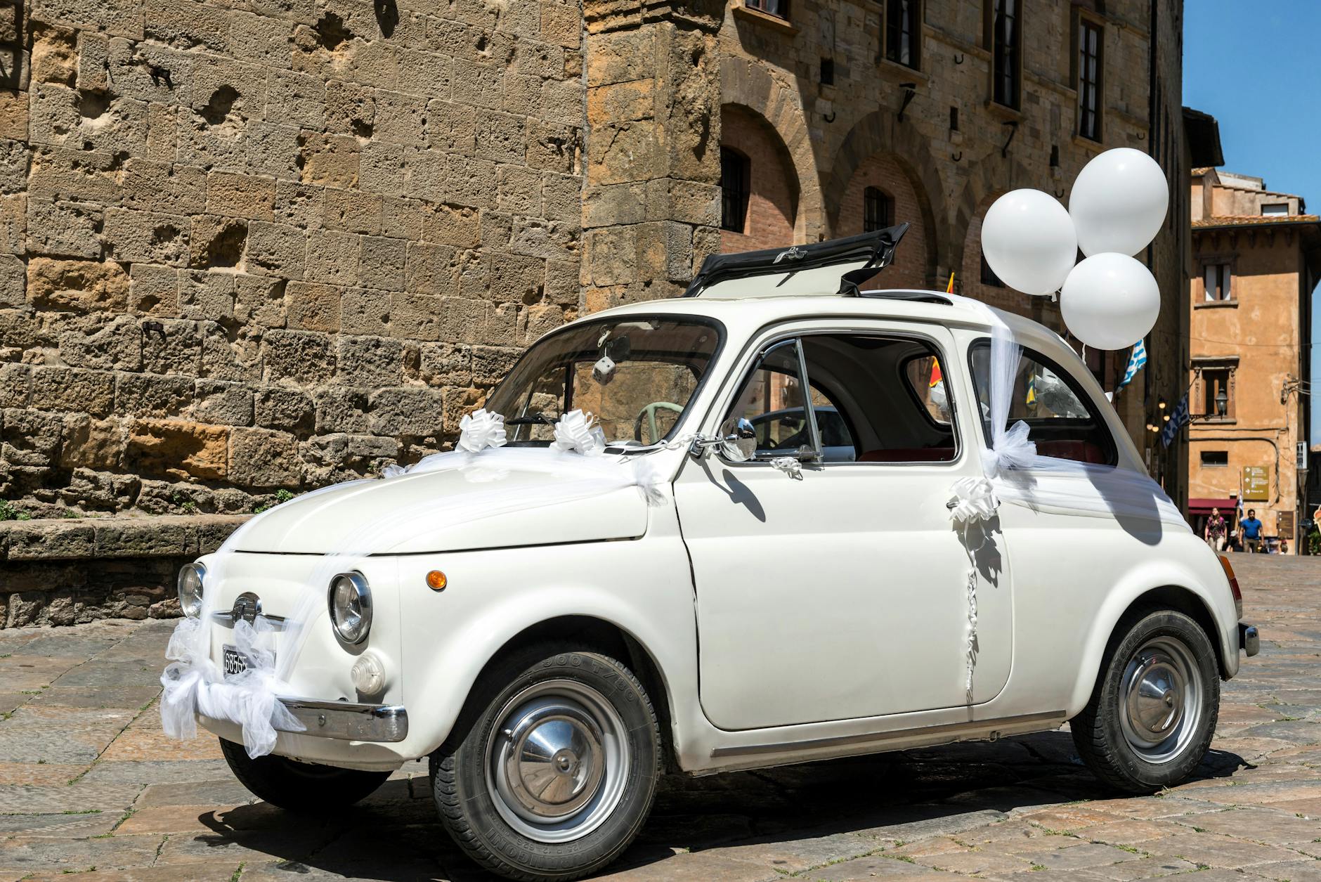 Fiat 500 ślubnie przystrojony na słonecznej uliczce w Volterze