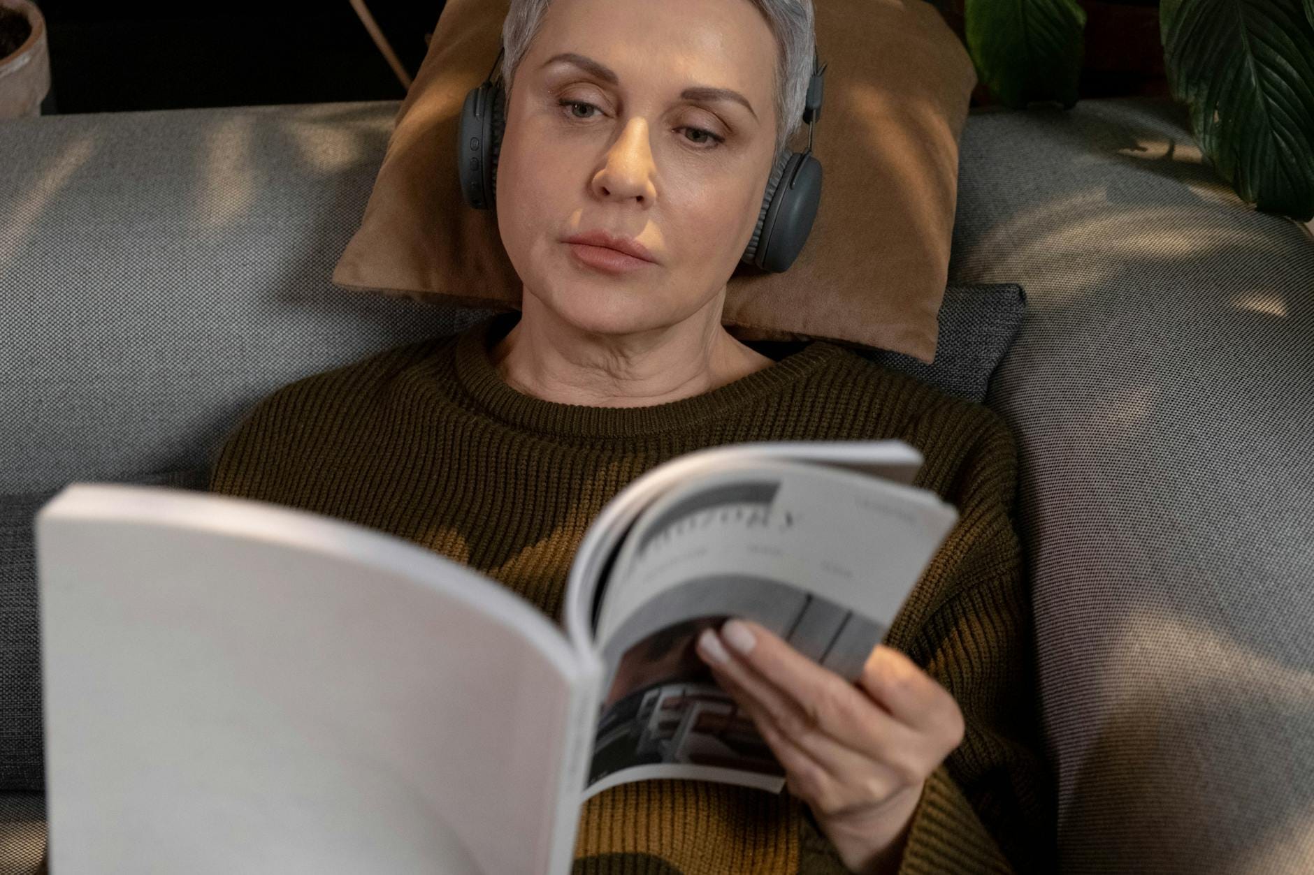 Kobieta w słuchawkach relaksuje się na kanapie i czyta magazyn
